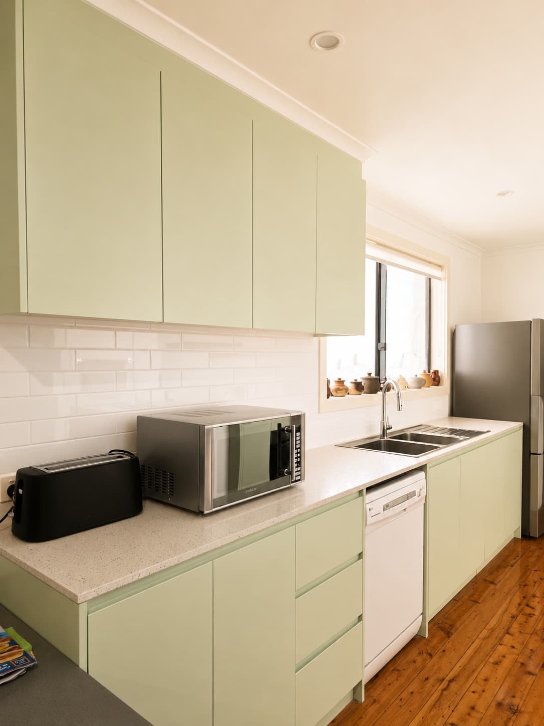 Sage green galley kitchen with white subway tile splashback by A&E Joinery